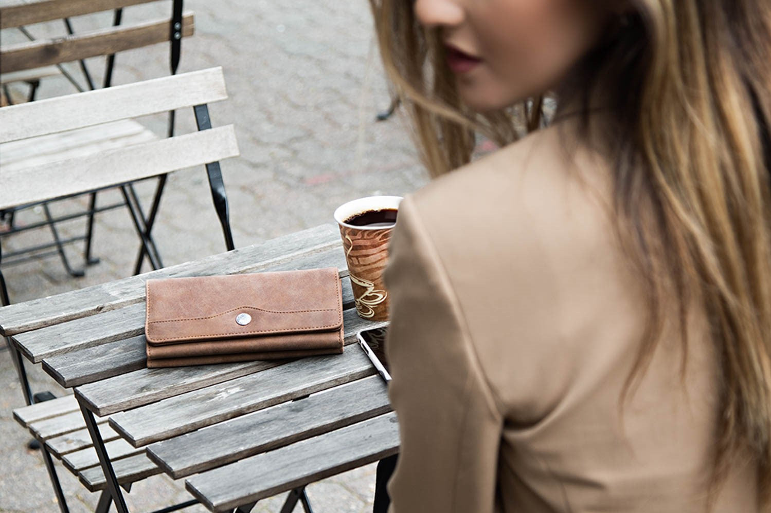 What is the Difference Between a Clutch and a Wallet? *A woman sits at a table with her brown file master clutch*